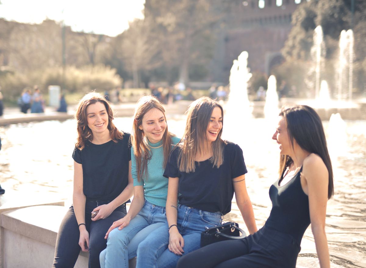 Four friends chatting and laughing by a fountain on a sunny day